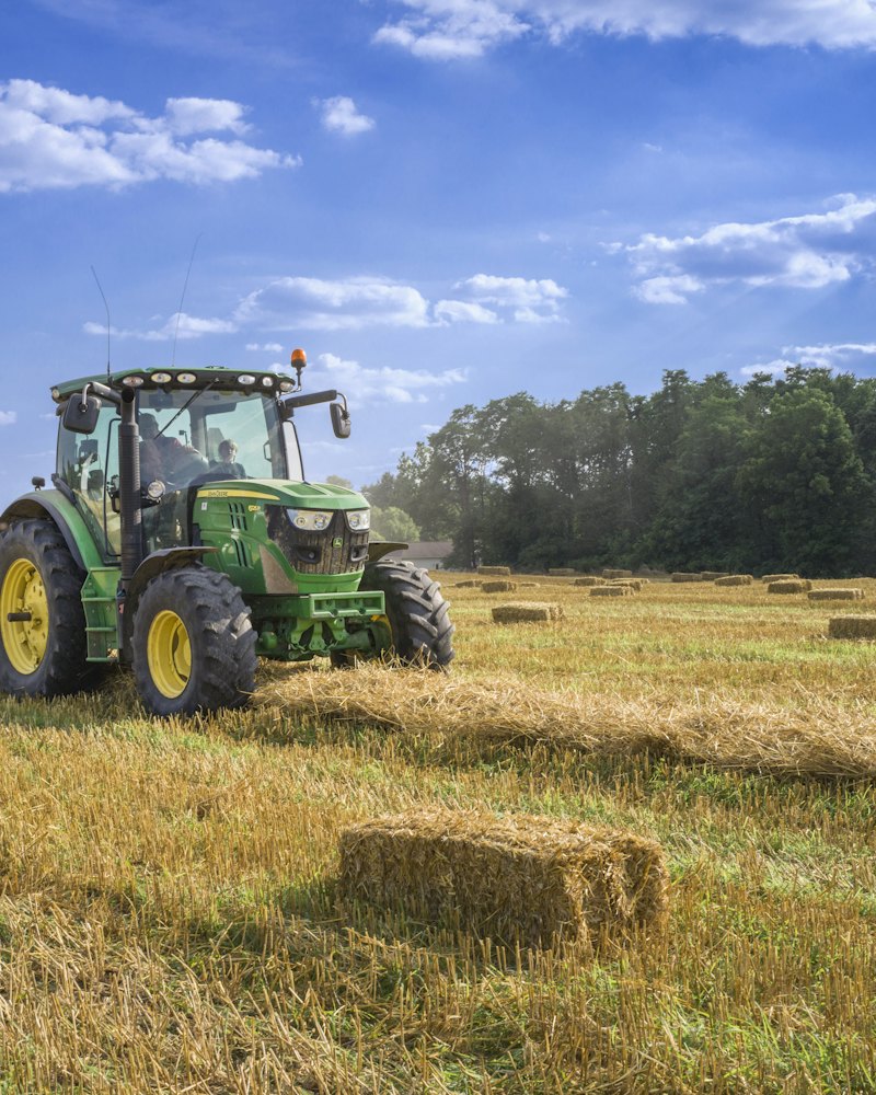 Green tractor in a field of freshly baled hay