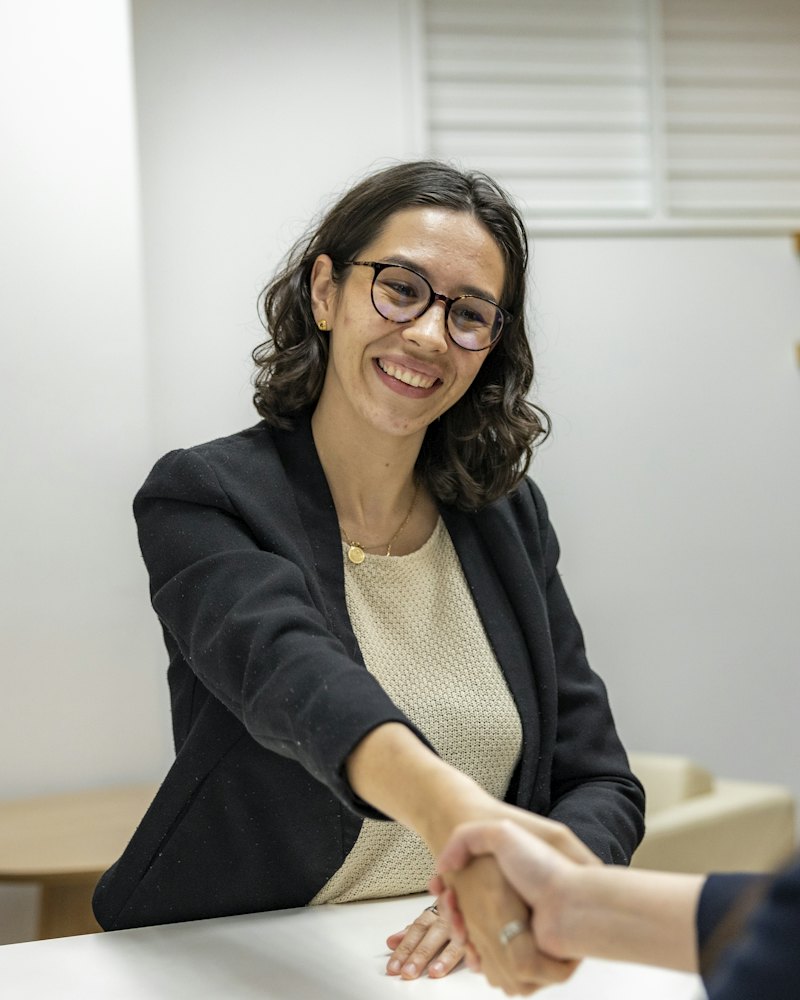 Two people shaking hands across a table at an interview