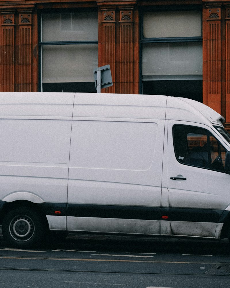 White panel van parked on a street outside a brick building
